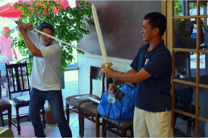 How-Lun Chen and Terry Fojas spar with corrugated cardboard model swords. Chen’s company Crafteeo produces DIY schematics for cardboard crafts for children and adults