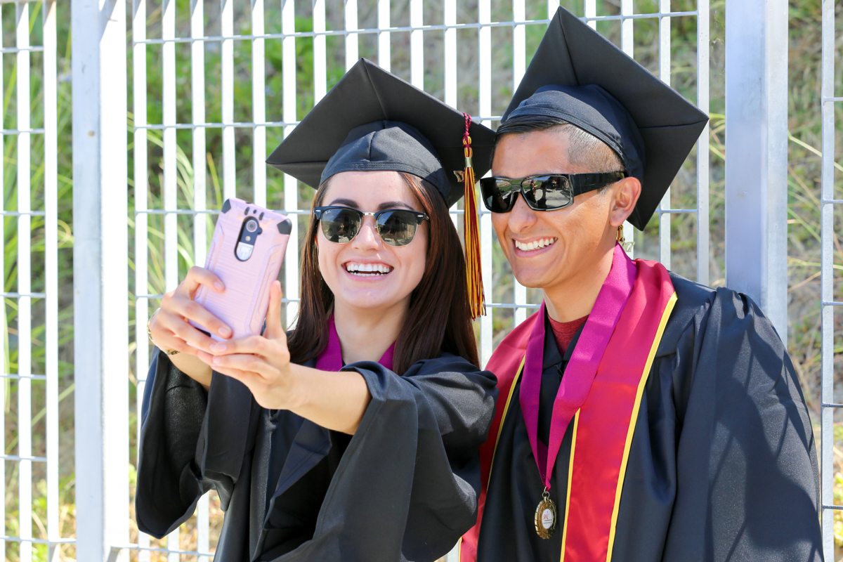 Two students in cap and gown smiling and taking a selfie