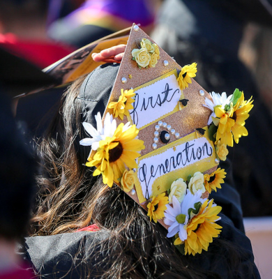 Graduate at Commencement wearing a graduation cap that reads "First Generation"